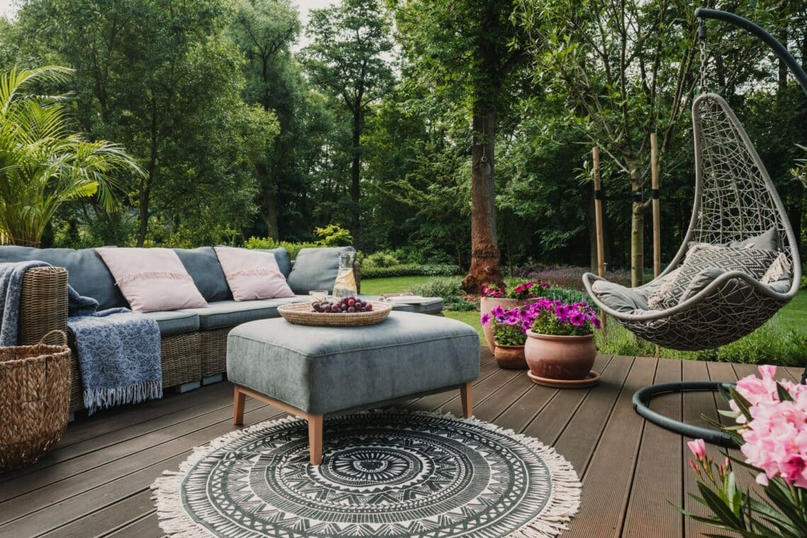 Stilvolle Sitzecke mit bequemen Sofas, einem Hängesessel und Blumentöpfen auf einer Holzterrasse, ideal für eine Garten-Oase neben Gartenpavillons.