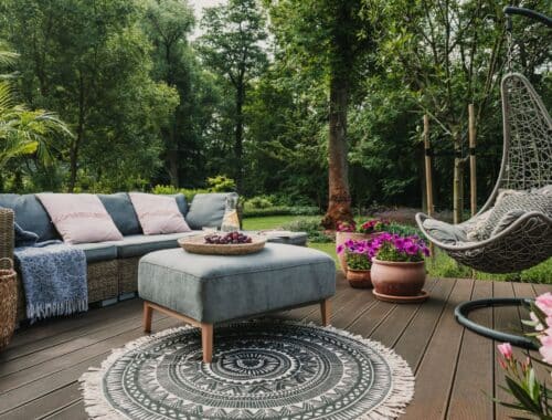 Stilvolle Sitzecke mit bequemen Sofas, einem Hängesessel und Blumentöpfen auf einer Holzterrasse, ideal für eine Garten-Oase neben Gartenpavillons.