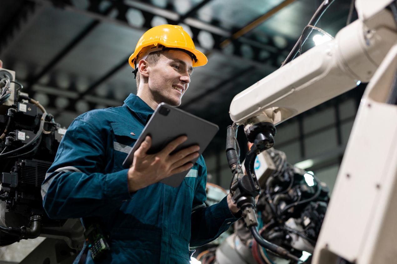 Techniker mit Tablet interagiert mit Roboterarm in Produktionshalle – echte Anwendung von Roboter Unternehmen in der Fertigung