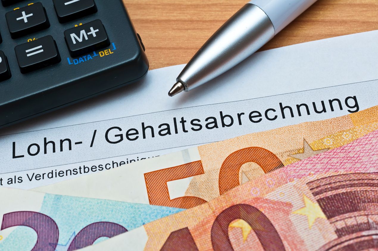 Geldscheine liegen auf Lohnabrechnung neben Taschenrechner im Lohnbüro