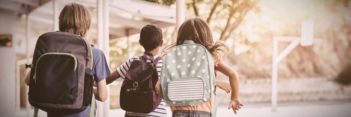 Drei Kinder mit Schulranzen auf dem Weg zur grundschule berlin bei Morgensonne