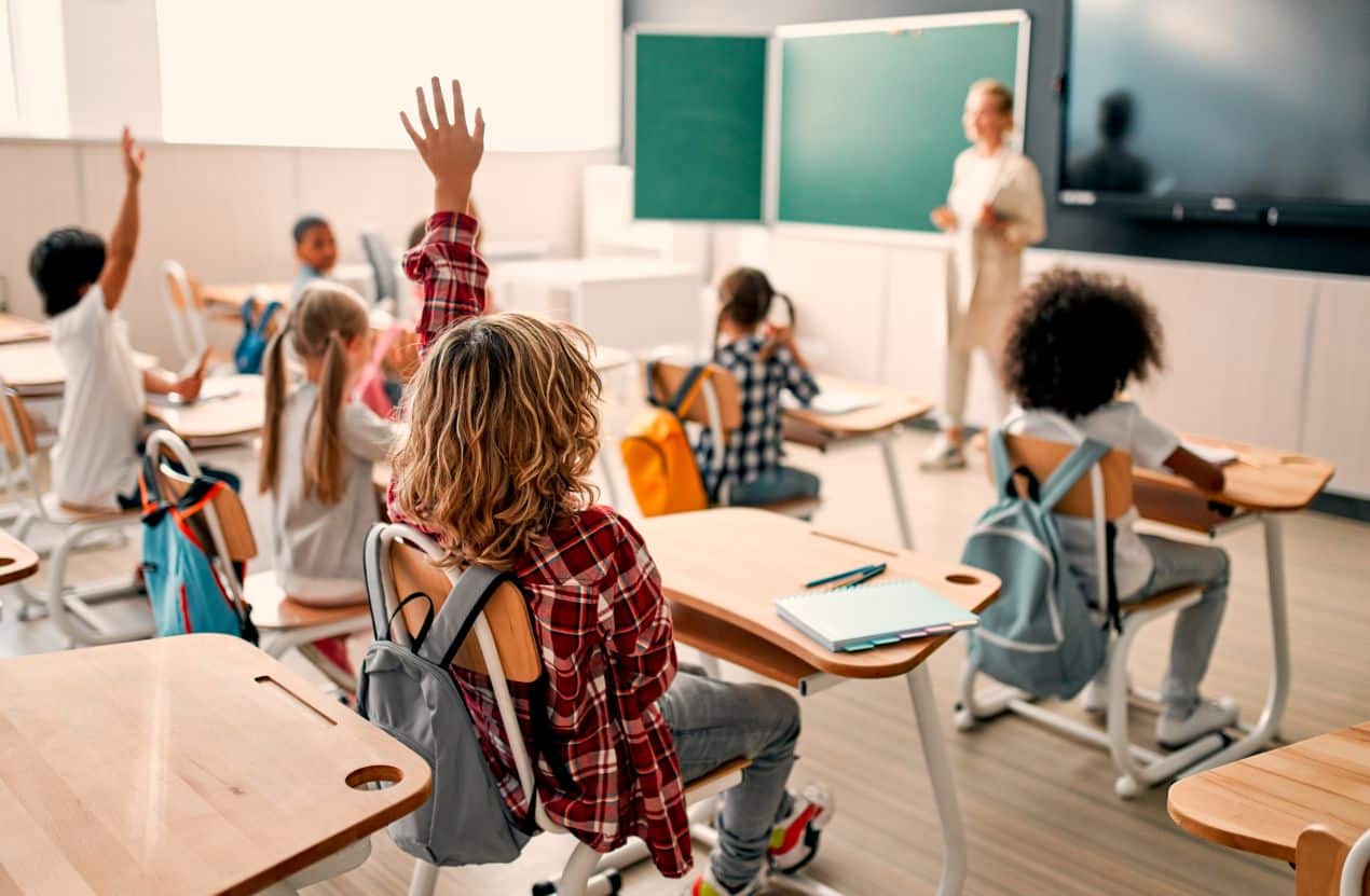 Schueler im modernen Klassenraum der grundschule berlin melden sich aktiv im Unterricht
