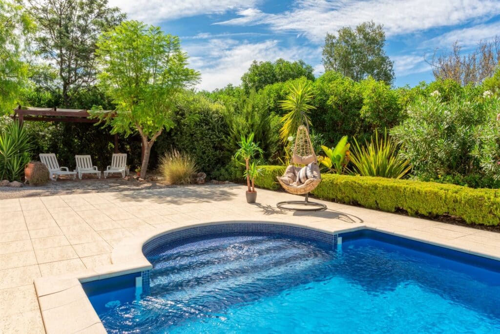 Blauer Garten Pool mit mediterranen Pflanzen, Liegestuehlen und sonnigem Aussenbereich